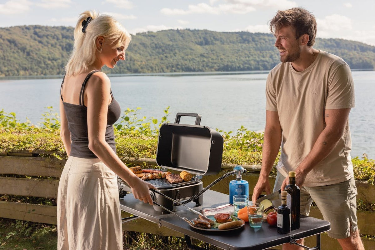 Svart hopfällbart campingbord med stålram som grillstation vid sjö