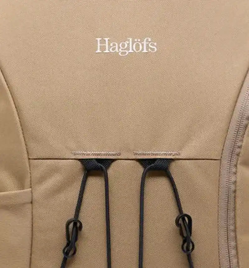 Detaljbild av beige vävmaterial med Haglöfs-logotyp och dragsnöror