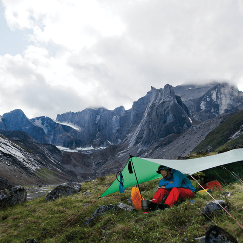 Person under grön Hilleberg Tarp 10 UL på bergig terräng med stavar
