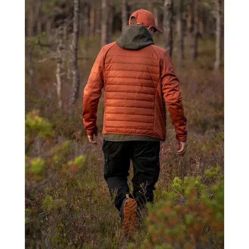 Man i orange vadderad jacka med huva som vandrar genom skogsmiljö