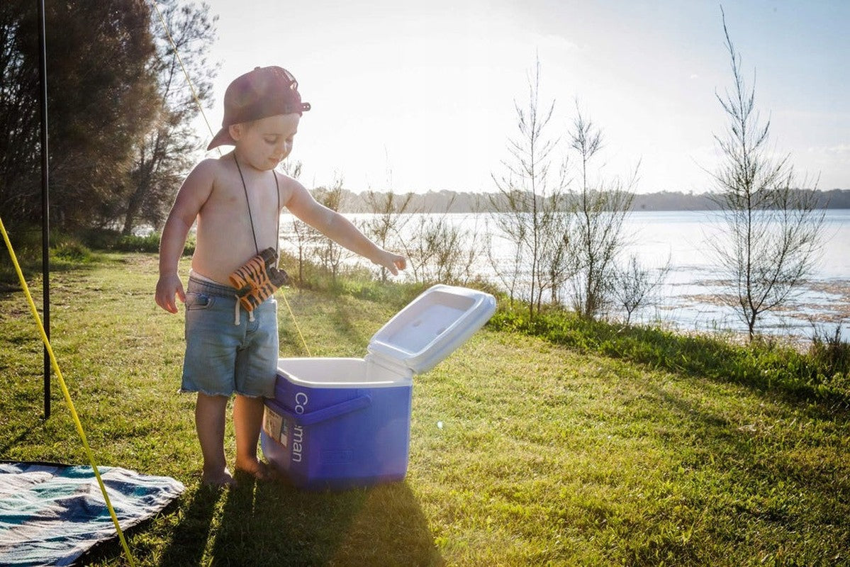 Pojke som öppnar blå kylväska vid sjön för picknick eller fiske