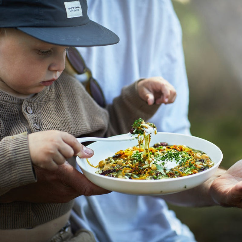 Barn äter med vit spork från skål utomhus