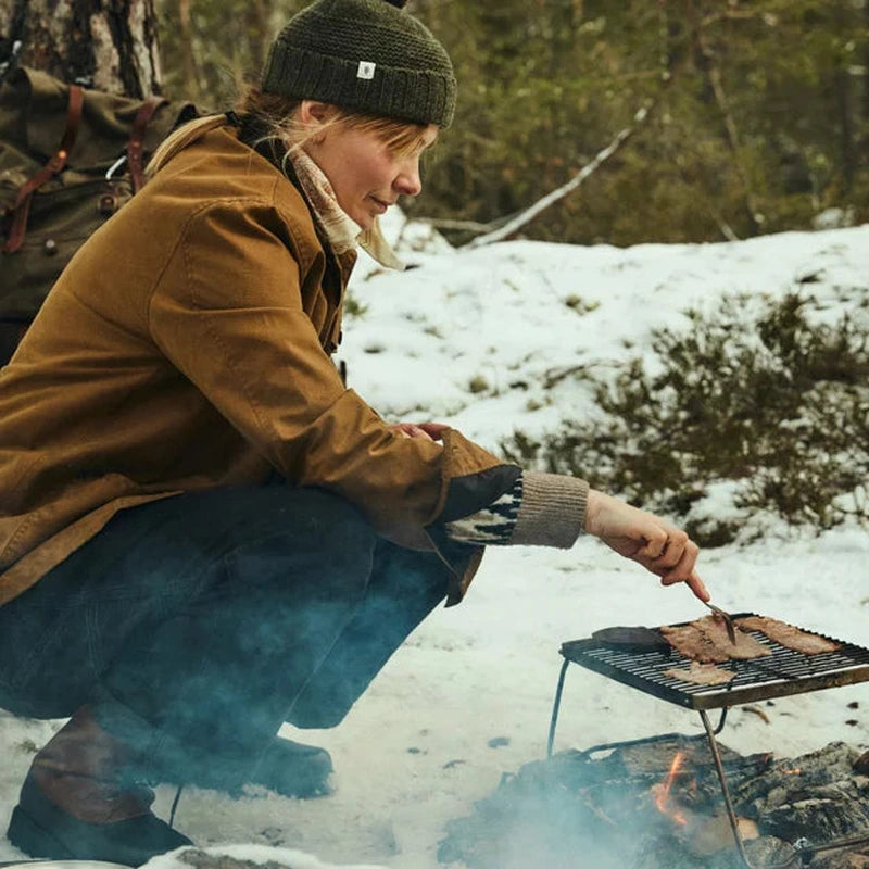 Kvinna knäböjer i snö med Graninge kängor vid grillställ