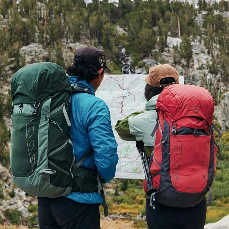 Par i skogsmiljö med mörkgrön och röd Osprey Tempest 33 ryggsäck under kartläsning i bergen