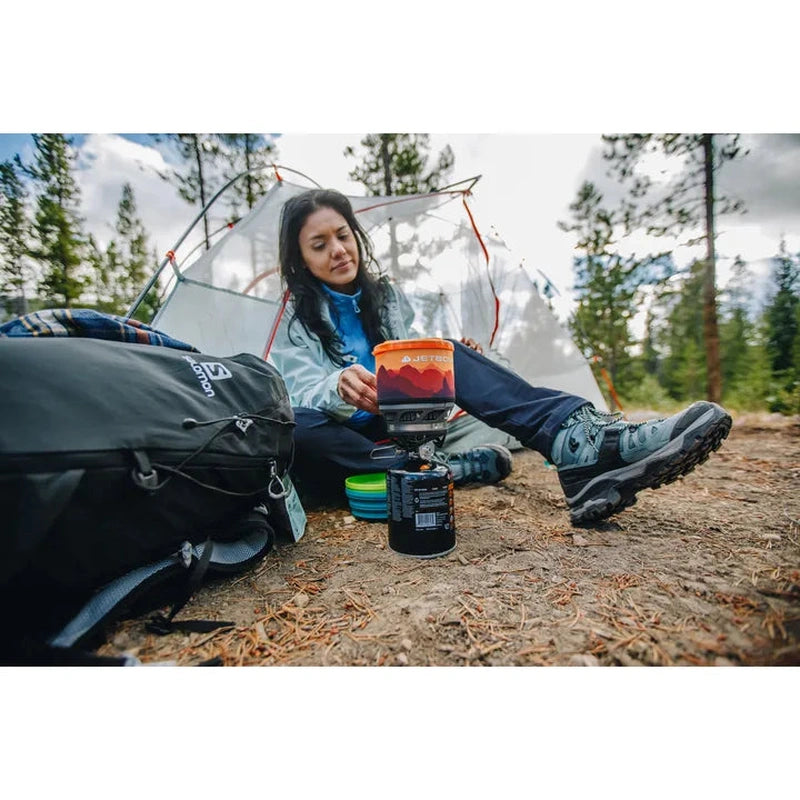 Kvinna vid lägerplats med Jetboil-kökssats bärande höga Salomon vandringskängor