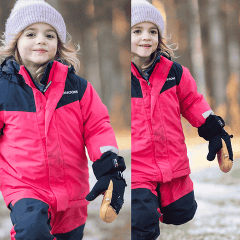 Barn går i snö med svarta Videmyr skidhandskar för lek i kyla