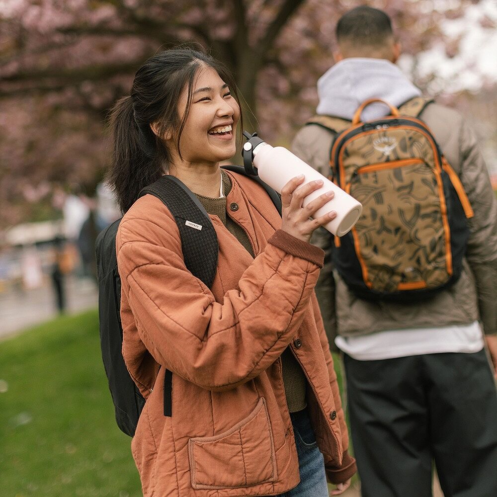 Kvinna utomhus med ryggsäck som håller ljusrosa Hydro Flask vattenflaska